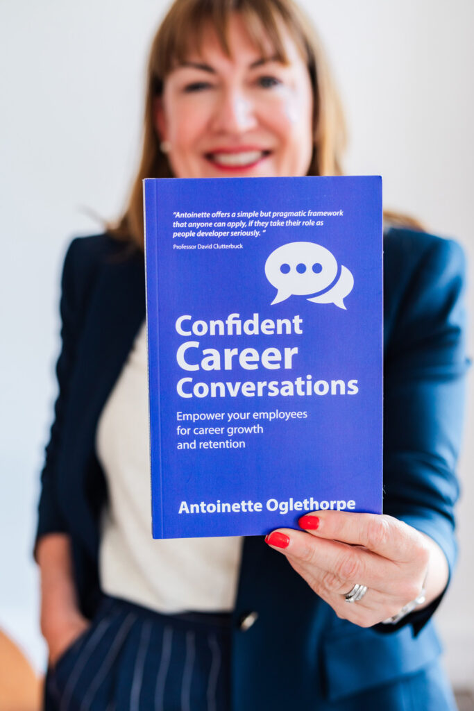 Antoinette Oglethorpe smiling in a business suit holds up a book titled 