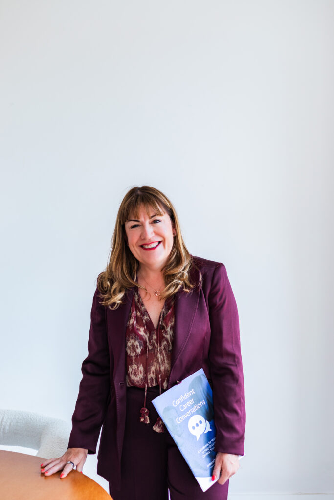 Antoinette Oglethorpe headshot, wearing a maroon suit stands and smiles, holding a booklet titled 