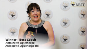 Antoinette Oglethorpe in a black dress holds a gold star trophy and smiles, standing in front of a 