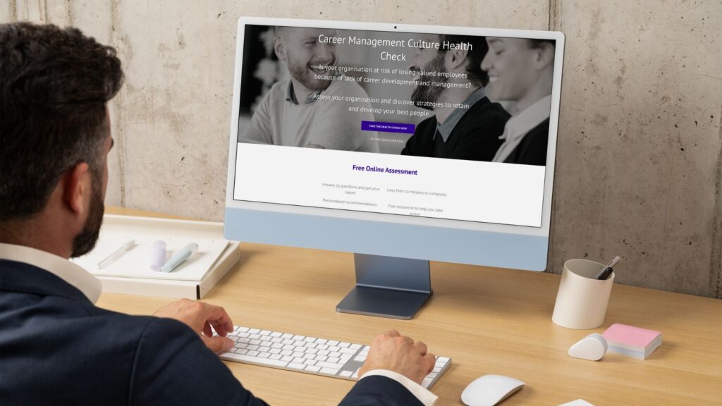 A man in business attire sits at a desk, typing on a keyboard and viewing a website titled 