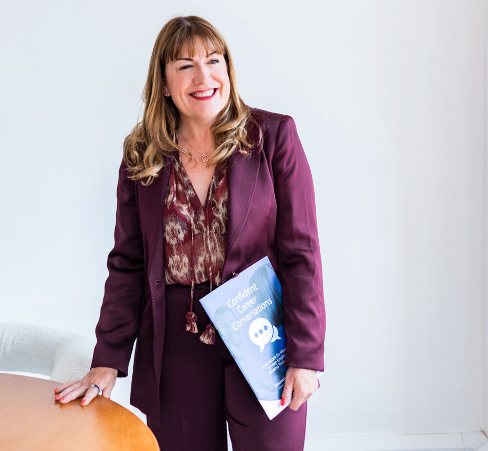 Antoinette Oglethorpe in a maroon suit stands smiling, holding a booklet titled 