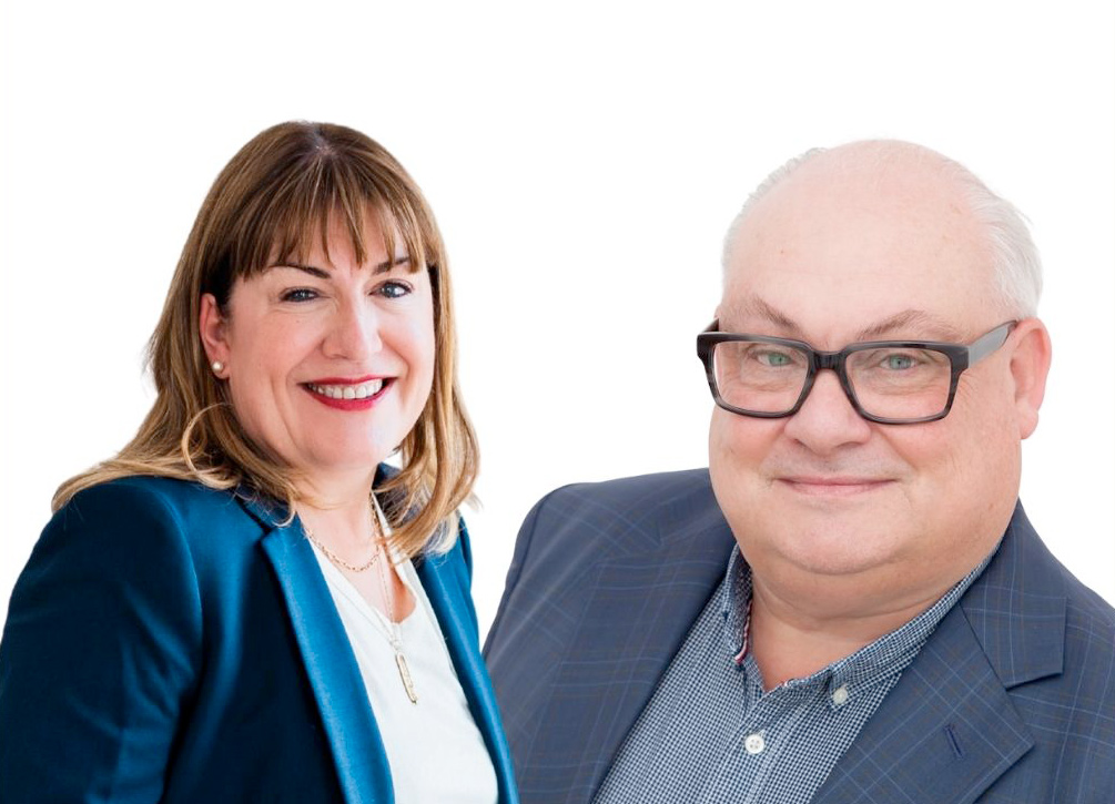 Antoinette Oglethorpe and Mark McKergow wearing business attire and smiling; Antoinette has shoulder-length brown hair and a blue blazer, while the Mark has glasses, short grey hair, and a checked jacket. Both are pictured against a white background. in t6he promotional bannewr for the webinar Solutions Focus and Mentoring