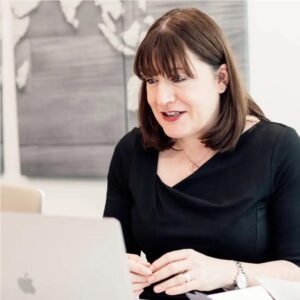 Antoinette Oglethorpe delivers the confident career conversations webinar wearing a black top, sits at a table and presents on a laptop. A world map wall art is visible in the background.