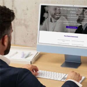 A man in business attire sits at a desk, typing on a keyboard and viewing a website titled 